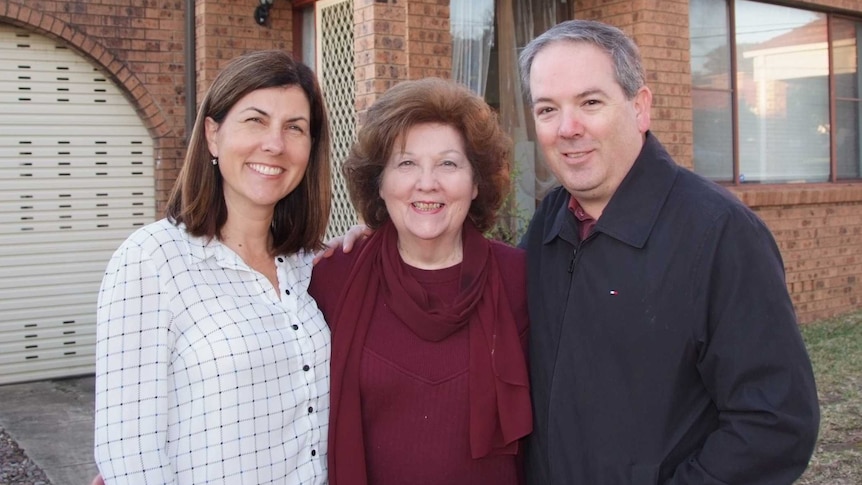 A mother and her two adult children outside the family home.