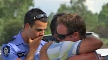 A police officer watches on as friends of the man killed in a ski boat accident on the Swan River console each other 20 January 2012