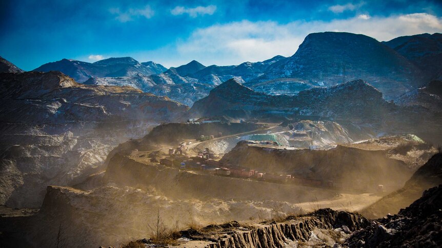Mining trucks driving through a coal mine site surrounded my mountains in China.
