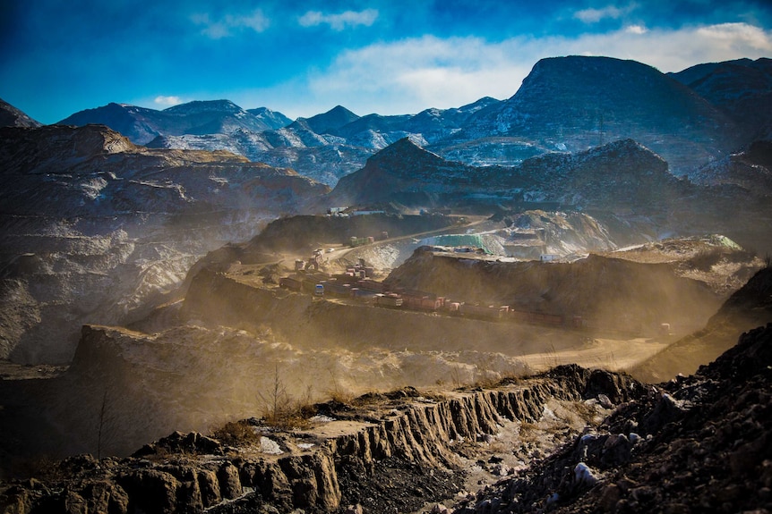 Mining trucks driving through a coal mine site surrounded my mountains in China.