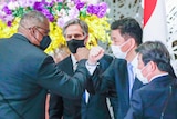 Four men elbow bumping while wearing face masks