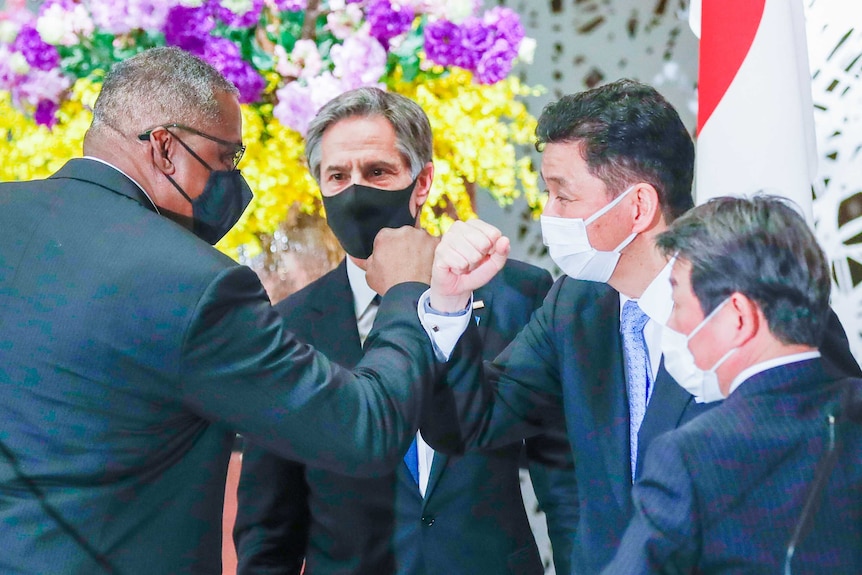 Four men elbow bumping while wearing face masks