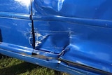A close up photo of the bottom of a blue car door which has been dented and the paint scratched in an accident.