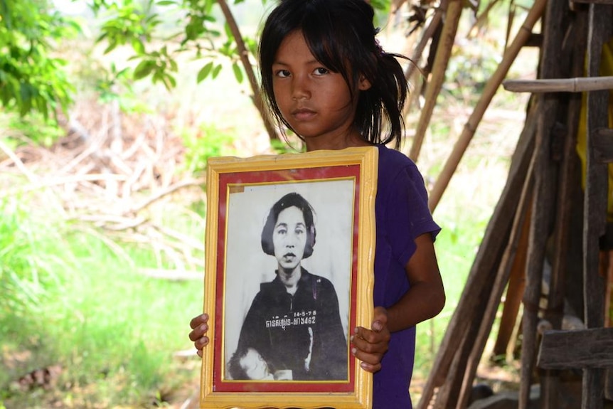 A black and white photo of a young Cambodian girl holding a portrait of her grandmother, who is holding a baby.