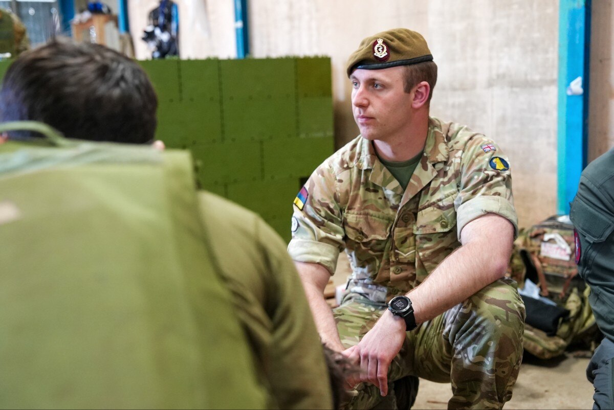 A man in a military uniform, crouching down and looking on.