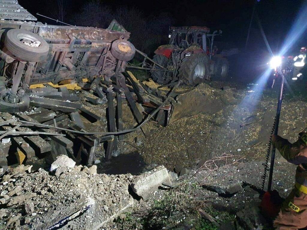 Vehicles tossed over and railing lies buckled and skewed above a crater from a missile strike at night