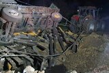 Vehicles tossed over and railing lies buckled and skewed above a crater from a missile strike at night