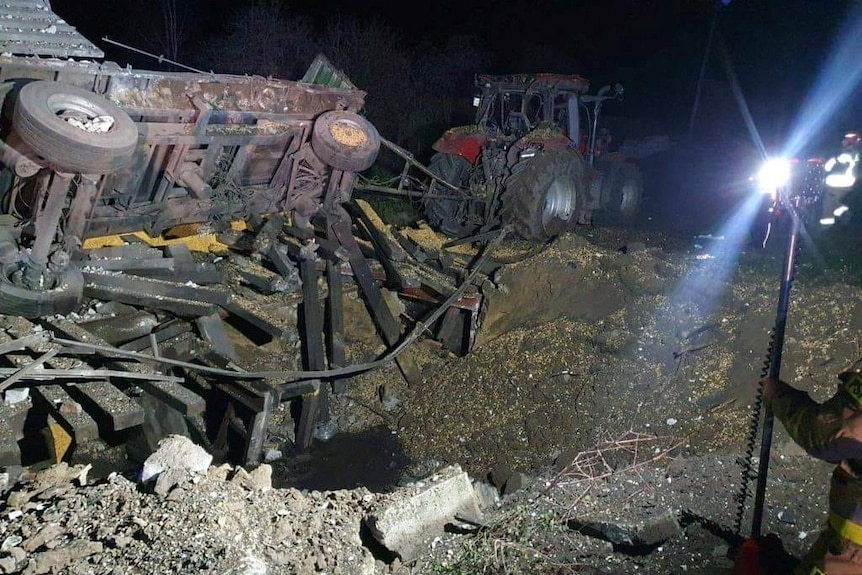 A destroyed tractor and trailer lie near an apparent missile crater with grain on the ground.