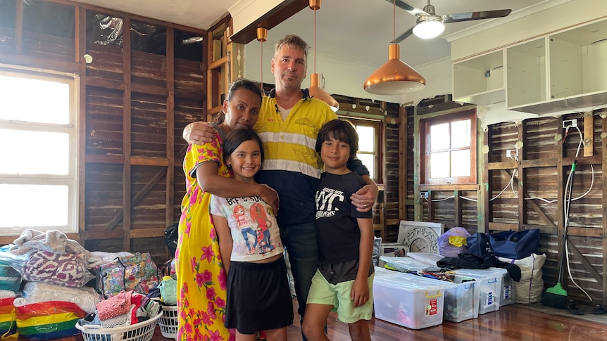 A man, woman and two kids with their arms around each other in a living area.