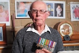 Elderly war veteran Norm Ginn in his home holding his service medals.