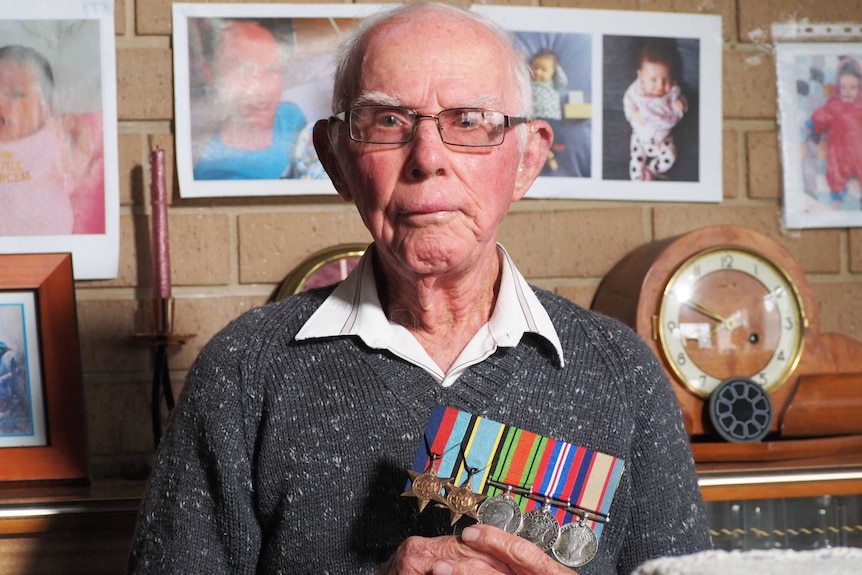 Elderly war veteran Norm Ginn in his home holding his service medals.