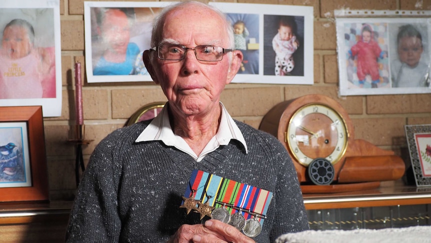 Elderly war veteran Norm Ginn in his home holding his service medals.