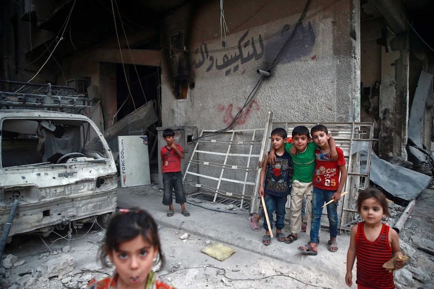 A group of Syrian children stand at the entrance to a damaged building.
