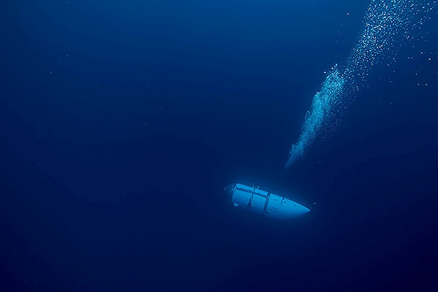 A dim, dark blue picture of a white submersible underwater, with a stream of bubbles coming from it.