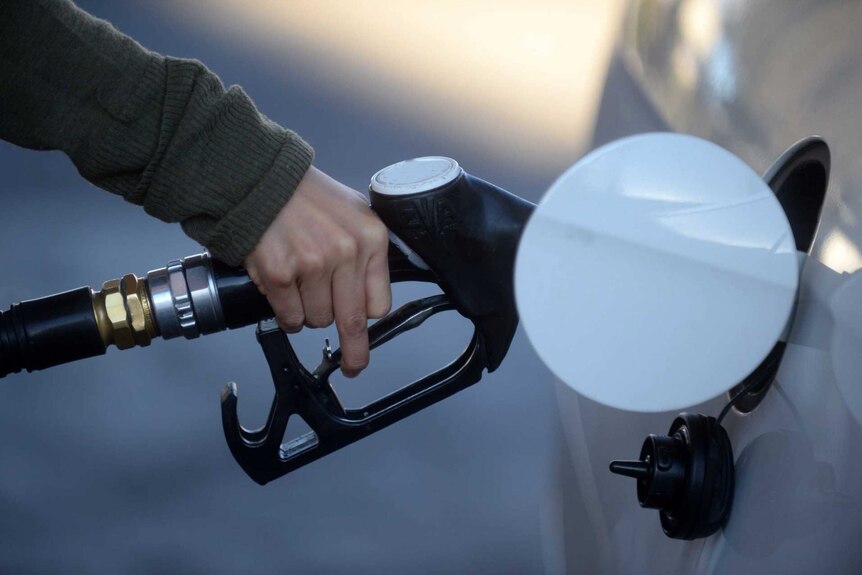 Ręka trzymająca dyszę paliwową, która wlewa benzynę do białego samochodu