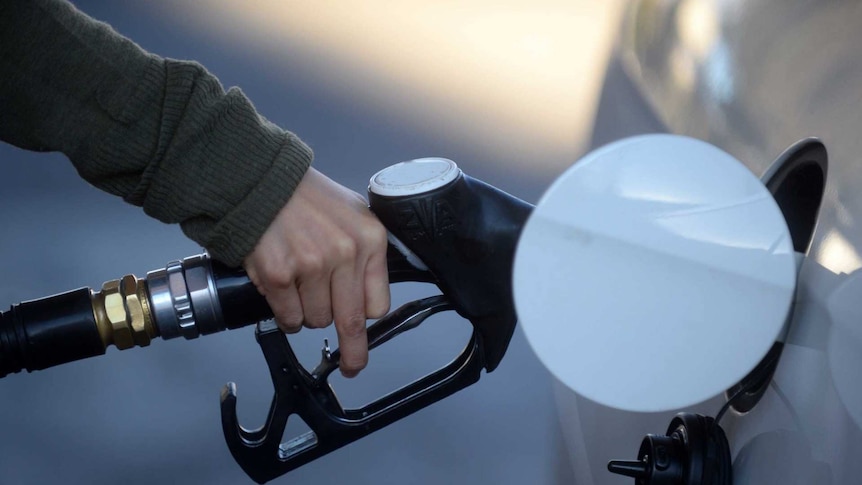 A hand holding a fuel nozzle putting petrol in a white car