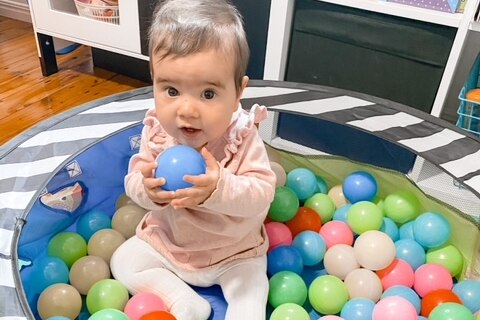 Baby Chloe sits in a ball pit.