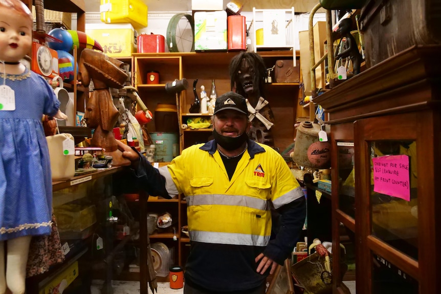 A man in a flat cap and high-vis shirt standing in a shop crammed with curios.