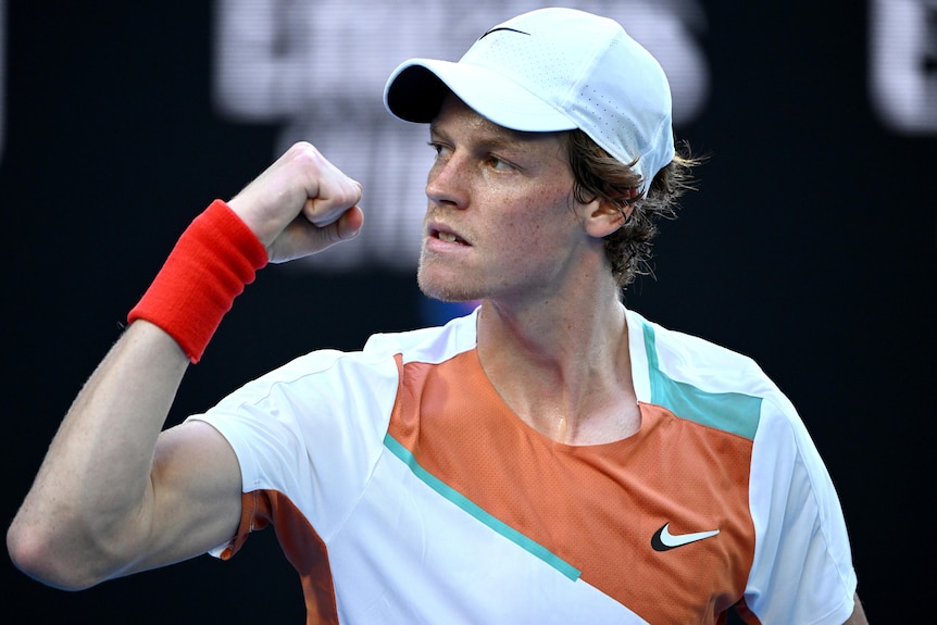 An Italian male tennis player raises his right arm as he celebrates winning a point.