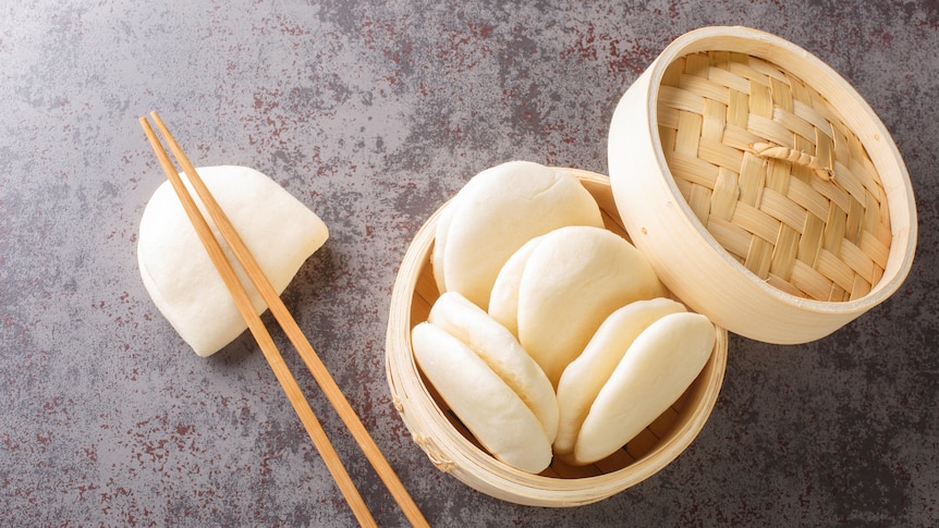 Little dough pockets, or bao buns, sit in a bamboo steamer.
