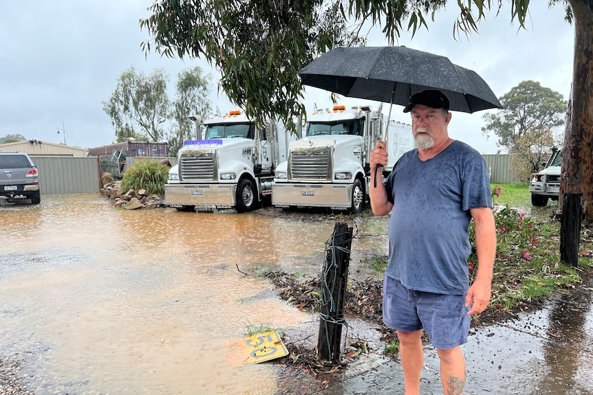 A man under an umbrella near flood water.