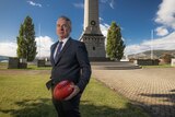 RSL Tasmania CEO John Hardy stands in front of the Hobart Cenotaph holding a football.