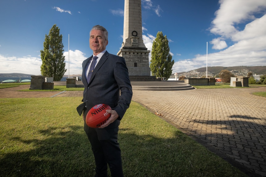 RSL Tasmania CEO John Hardy stands in front of the Hobart Cenotaph holding a football.