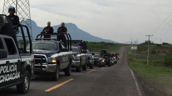 Black SUVs driving on a road with armed men in the tray.