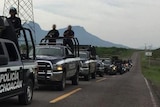 Black SUVs driving on a road with armed men in the tray.