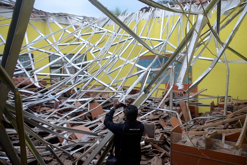 pieces of a damaged classroom roof are filmed by a man with a camera