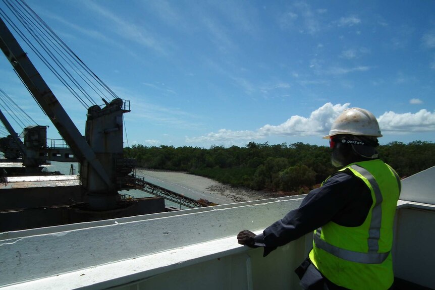 Tiwi Plantations Corporation chairman Kim Puruntatameri wears a high vis vest and helmet as he stand on ship's bridge.