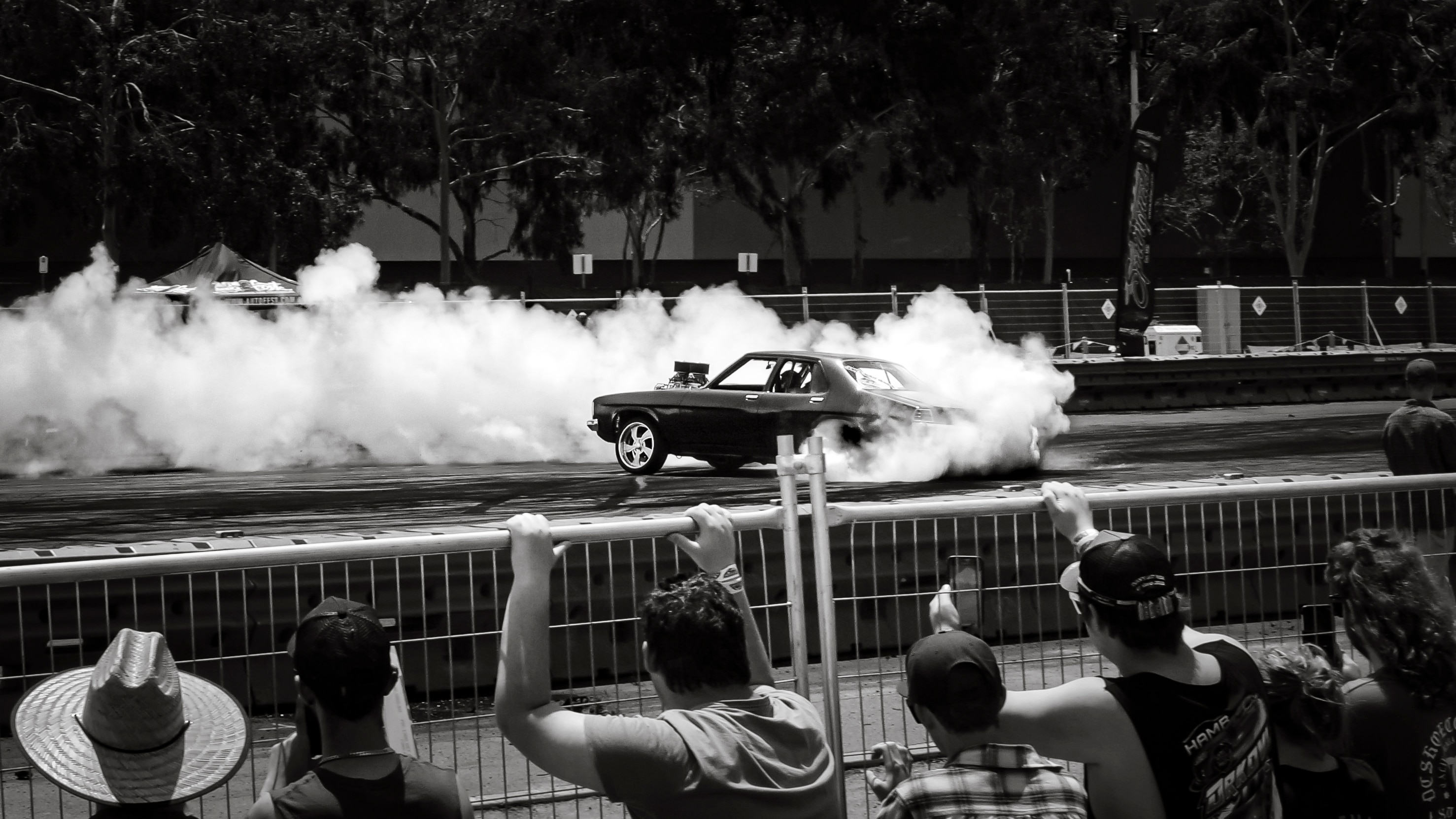 spectators watch a car doing burnouts from behind a metal fence and barricades