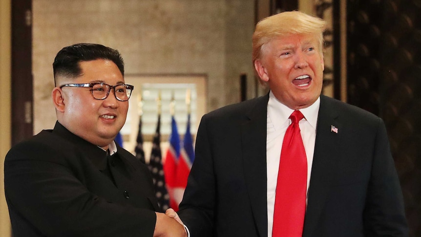 Kim Jong-un and Donald Trump shake hands and smile.