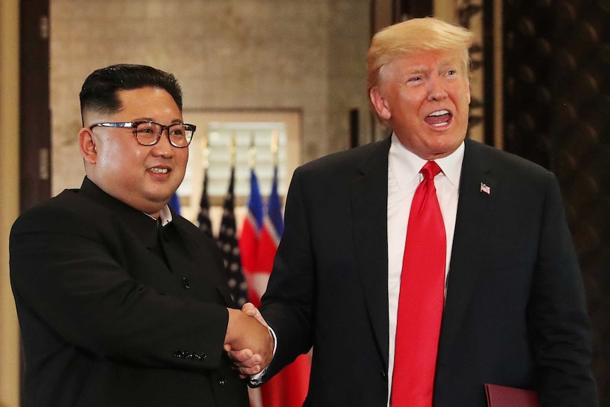 Kim Jong-un and Donald Trump shake hands and smile.