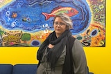 A woman stands in front of a colourful painting.