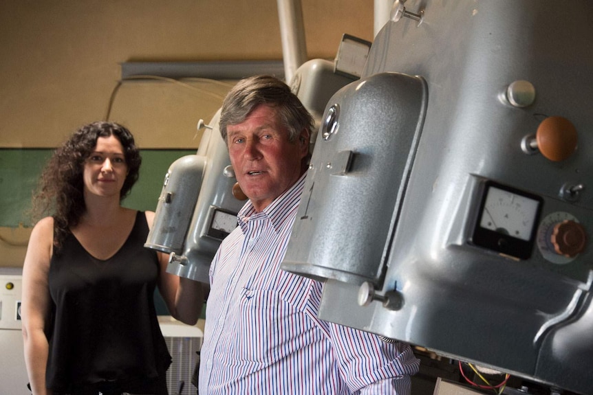 A man and woman standing next to huge old movie projectors