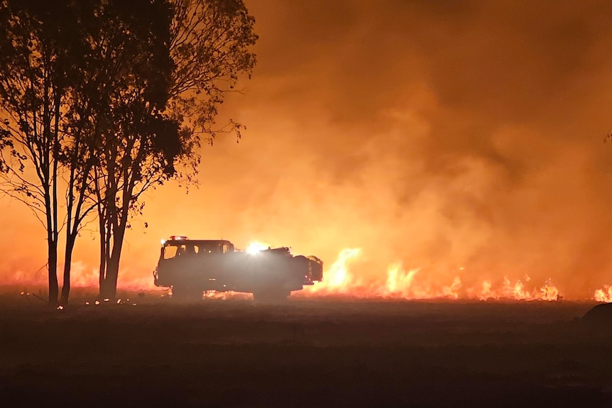 A fire vehicle backlit by an intense blaze
