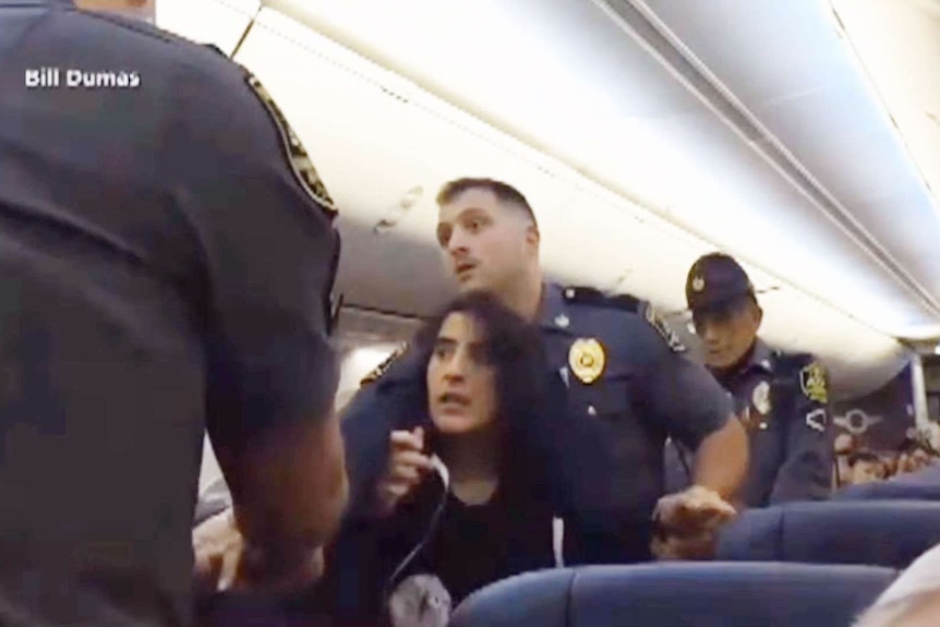 Police struggle with a woman in the aisles of a plane.