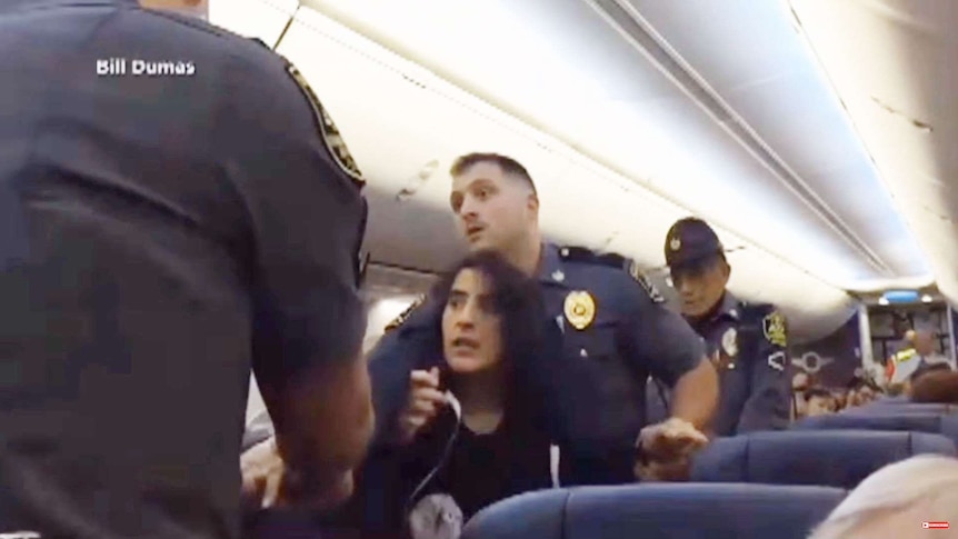 Police struggle with a woman in the aisles of a plane.