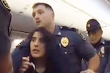 Police struggle with a woman in the aisles of a plane.