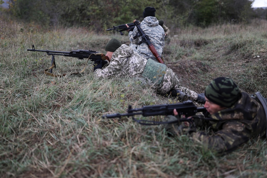 Soldiers aim rifles while crouching among grass in the Krasnodar region of Russia 