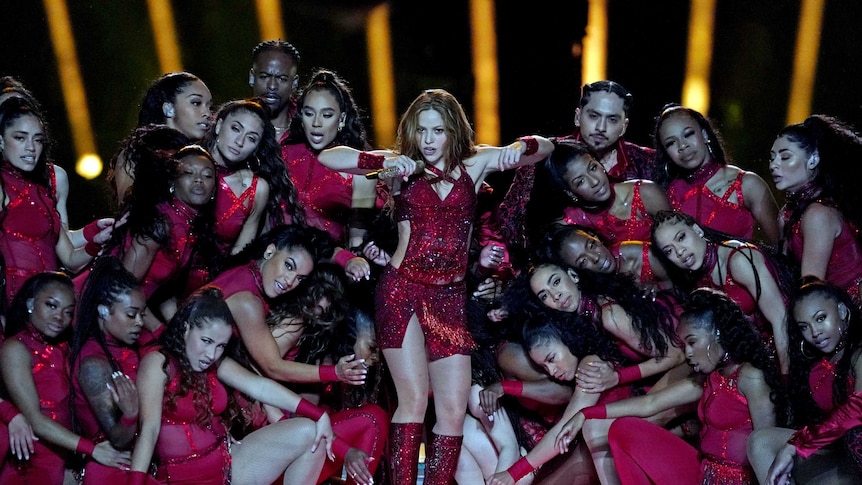 A woman standing in the middle of dancers all dressed in red