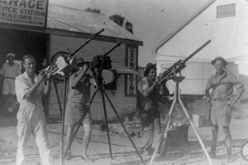 Men stand with large machine guns on tripods.