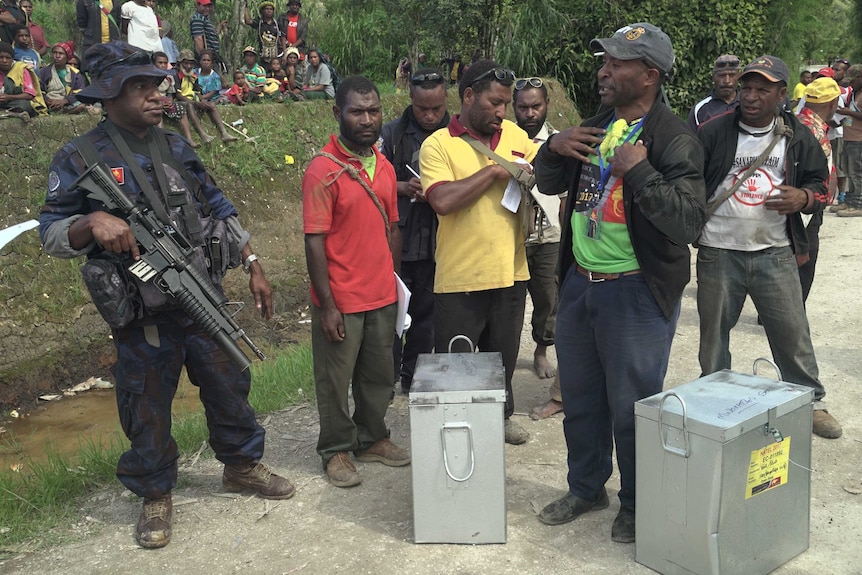 An armed police officer and a polling official stand with two recovered ballot boxes that were stolen by voters.