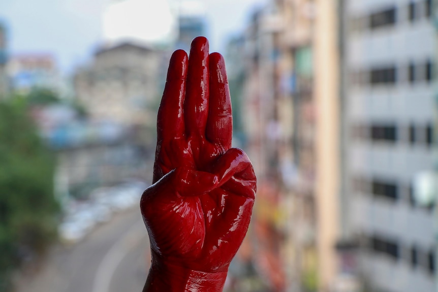 An anti-coup protester shows the three fingered salute of resistance on his red painted hand