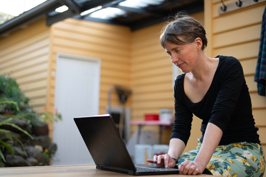 A young lady sits out on the deck and is using her laptop.