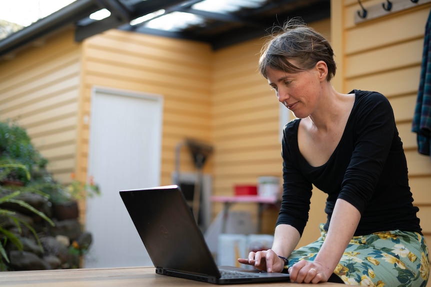 A young lady sits out on the deck and is using her laptop.