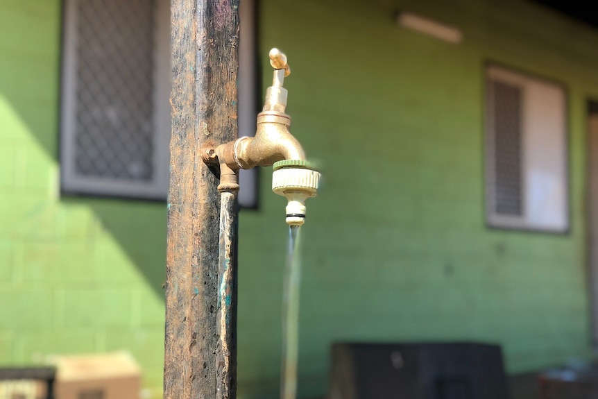 A running tap, pictured in front of a green house