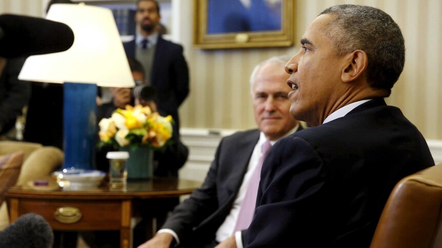 Malcolm Turnbull, slightly out of focus, looks and listens to Barack Obama speaking in the Oval Office.