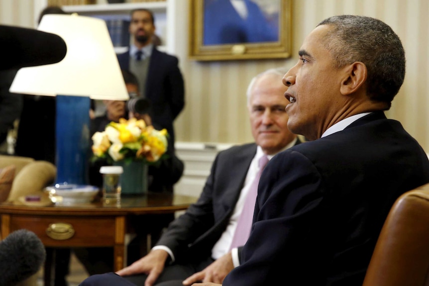 Malcolm Turnbull, slightly out of focus, looks and listens to Barack Obama speaking in the Oval Office.